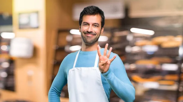 Man wearing an apron happy and counting four with fingers in a bakery