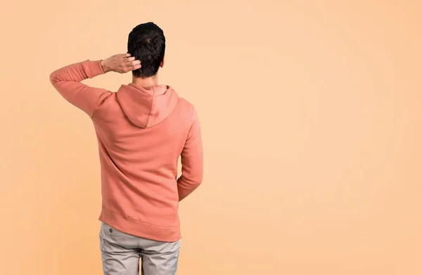 Man in a pink sweatshirt looking back on ocher background