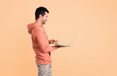 Pembe bir kazak koyu sarı arka plan üstünde laptop ile adam