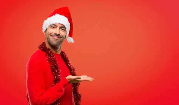 Man with red clothes celebrating the Christmas holidays presenting an idea while looking smiling towards on red background