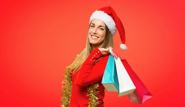 金发碧眼的女人打扮成圣诞节假期 在红色背景上拿着很多购物袋 — 图库照片