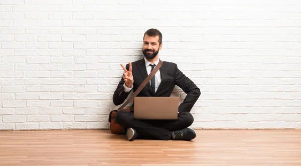 Businessman with his laptop sitting on the floor happy and counting two with fingers