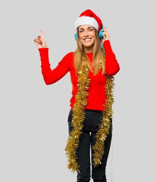 金发碧眼的女人打扮圣诞节假期听音乐与耳机和舞蹈在孤立的灰色背景 — 图库照片
