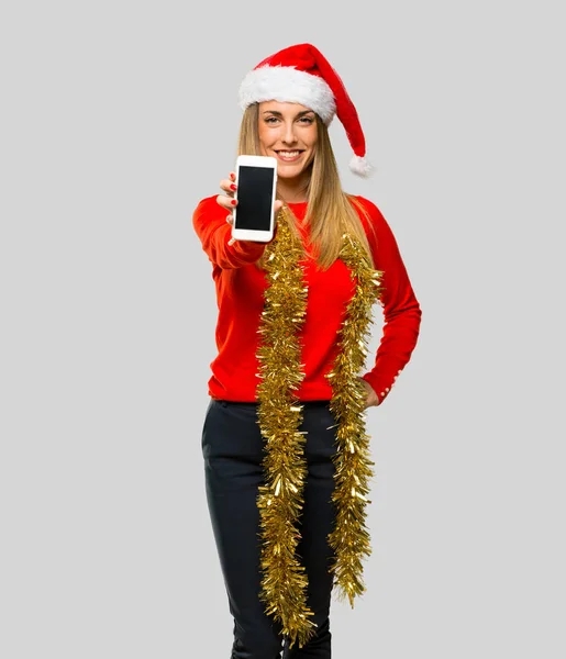 金发碧眼的女人打扮圣诞节假期看着相机 微笑着 同时使用手机在孤立的灰色背景 — 图库照片