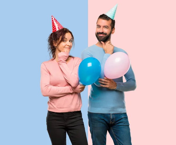 couple with balloons and birthday hats smiling and looking to the front with confident face on pink and blue background