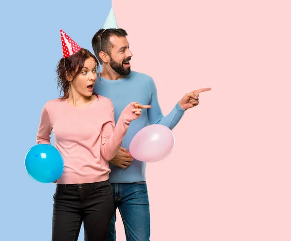 Pareja Con Globos Sombreros Cumpleaños Apuntando Con Dedo Hacia Lado —  Fotos de Stock