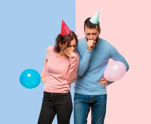 一对夫妇与气球和生日帽子是痛苦的咳嗽和感觉不好粉红色和蓝色的背景 — 图库照片