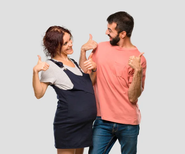 親指ジェスチャーと笑顔を与えるため妊娠中の女性とカップルが孤立した灰色の背景で成功を収めています — ストック写真