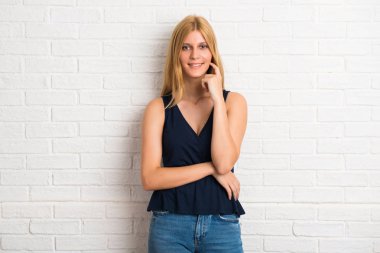 Gülümseyen ve öne doğru emin yüz ile beyaz tuğla duvar arka plan üzerinde seyir sarışın kadın