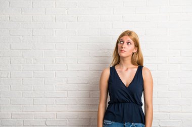 Sarışın kadın stand ve beyaz tuğla üzerinde ciddi yüzle ararken arka plan duvar