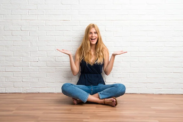 Blond Meisje Zittend Vloer Verrast Geschokt Gelaatsuitdrukking Witte Bakstenen Muur — Stockfoto