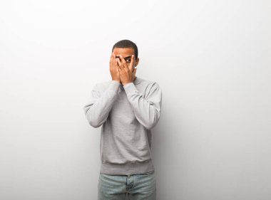 Afrika kökenli Amerikalı adam eliyle gözlerini kapsayan ve parmaklarının arasından seyir beyaz duvar arka plan üzerinde