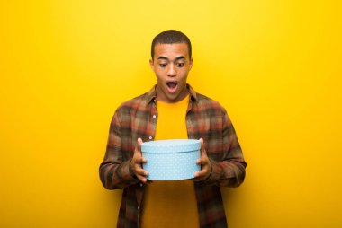 Hediye tutarak canlı sarı zemin üzerine genç Afro-Amerikan adam elinde kutuları