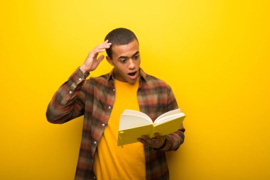 Bir kitap ve okuma tadını çıkarırken sürpriz canlı sarı zemin üzerine genç Afro-Amerikan adam