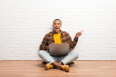 Afro-Amerikan erkek tarafına parmak işaret ve bir ürün sunan onun laptop ile katta oturan