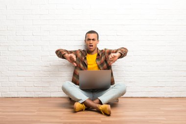 Afrika kökenli Amerikalı adam iki eliyle onun laptop gösteren başparmak ile katta oturuyor