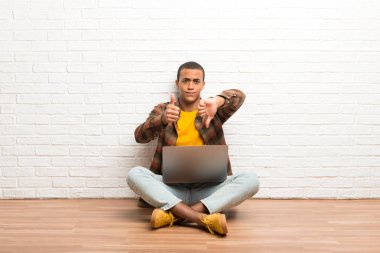 Afrika kökenli Amerikalı adam iyi-kötü işaret yapma onun laptop ile yere oturma. Arasında kararsız Evet ya da değil