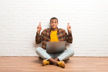 En iyi dilek ve geçiş parmakları ile onun laptop ile katta oturan Afrikalı-Amerikalı adam