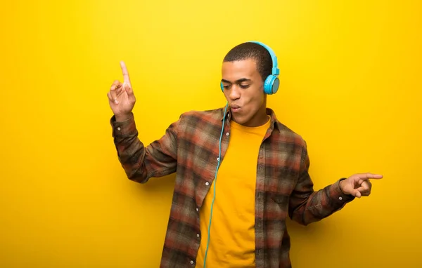 鮮やかな黄色の背景のヘッドフォンで音楽を聴くと踊りの若いアフリカ系アメリカ人 — ストック写真