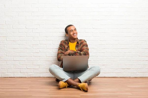 非洲裔美国人坐在地板上 他的笔记本电脑抬头 而微笑 — 图库照片