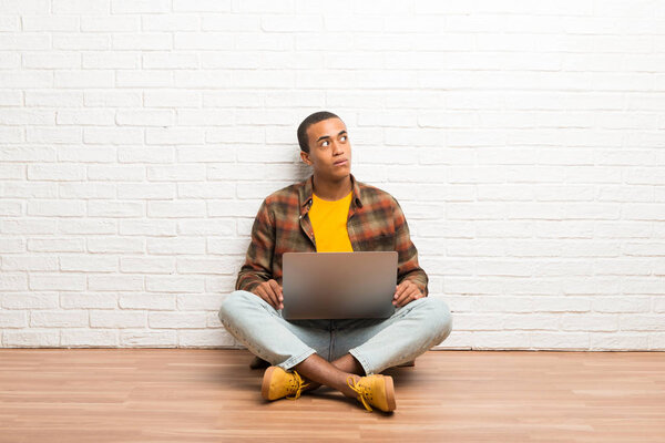 African american man sitting on the floor with his laptop looking up with serious face