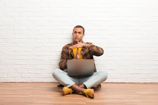 African american man sitting on the floor with his laptop making stop gesture with her hand to stop an act