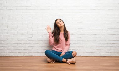 Mutlu ifade ile el ile selamlayan bir odada katta oturan genç kız