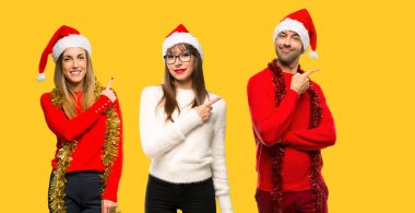 Sarı arka plan üzerinde bir ürün sunmak için parmağını bile yanında işaret Noel tatili için bir grup kişiye sarışın kadın giyinmiş