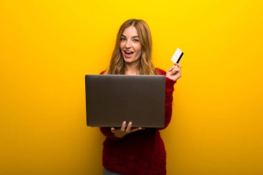 Laptop ve kredi kartı ile canlı sarı zemin üzerine genç kız