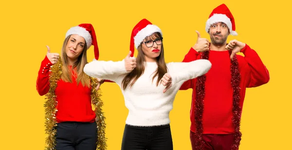 A group of people Blonde woman dressed up for christmas holidays making good-bad sign. Undecided between yes or not on yellow background