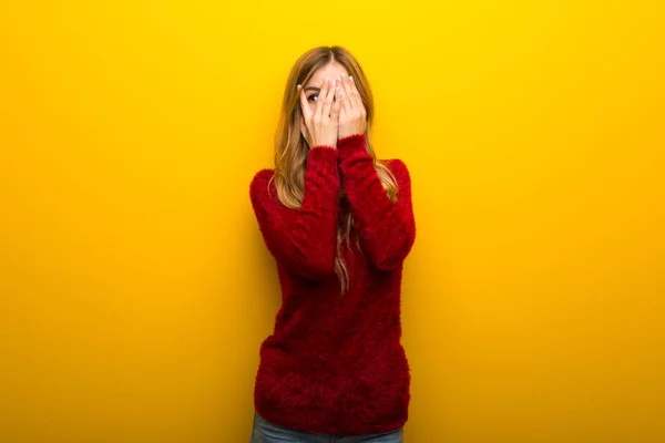 鮮やかな黄色の背景の手で目を覆っていると 指の間から見て若い女の子 — ストック写真