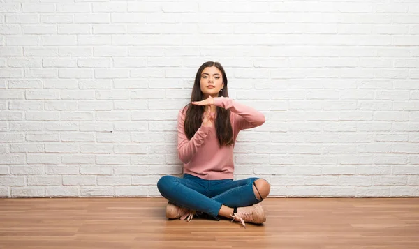 Teenager girl sitting on the floor in a room making stop gesture with her hand to stop an act