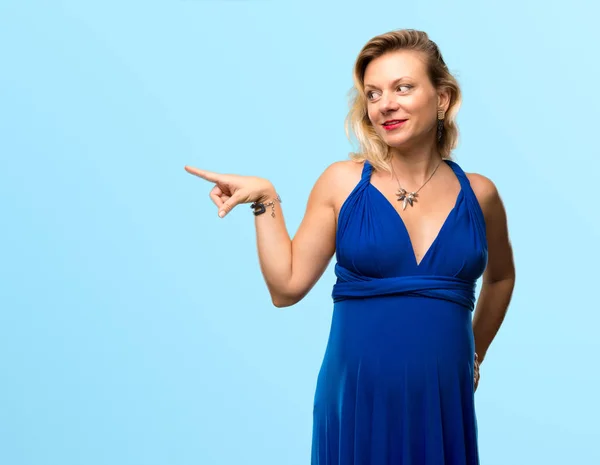 金髪妊婦青いドレス側に指を指していると分離の青い背景に製品を提示 — ストック写真
