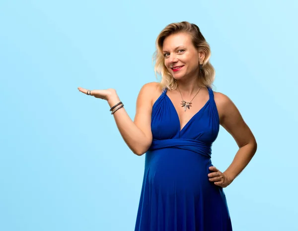 分離の青い背景に手のひらに架空 Copyspace を保持している青いドレスで金髪妊婦 — ストック写真