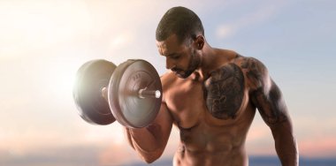 Halter yapma ve pazı günbatımı arka plan üzerinde egzersiz güçlü yakışıklı spor adamı