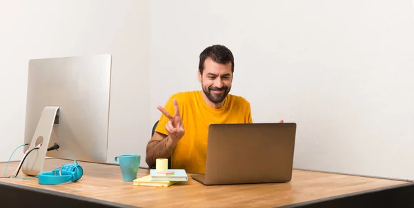 Чоловік Працює Ноутбуком Офісі Посміхається Показує Знак Перемоги Обома Руками — стокове фото