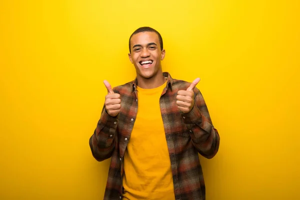 鮮やかな黄色の背景両手でジェスチャーを親指を与えると笑顔の若いアフリカ系アメリカ人 — ストック写真