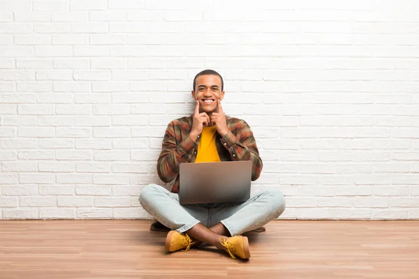 非洲裔美国人坐在地板上 他的笔记本电脑微笑着 愉快和愉快的表情 — 图库照片