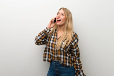 Sarışın genç kız cep telefonu ile bir konuşma tutmak beyaz duvar üzerinde