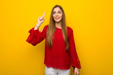 Genç kız sarı duvar niyetinde üzerinde kırmızı elbise ile çözüm parmak kaldırma sırasında fark eder