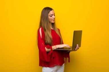 Dizüstü bilgisayar ile sarı duvarın üzerinden kırmızı elbise ile genç kız