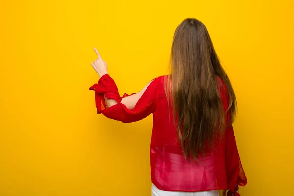 Νεαρό Κορίτσι Κόκκινο Φόρεμα Πάνω Από Κίτρινο Τοίχο Δείχνοντας Δάχτυλο — Φωτογραφία Αρχείου
