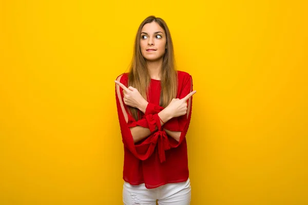 Menina Com Vestido Vermelho Sobre Parede Amarela Apontando Para Laterais — Fotografia de Stock