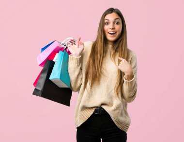 Alışveriş torbaları ile izole pembe bir arka plan üzerinde sürpriz yüz ifadesi ile genç kız