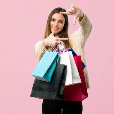 Genç kız ile alışveriş torbaları yüz odaklanarak. İzole pembe arka plan sembolü çerçeveleme