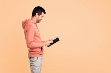 Pembe bir kazak tutarak ve koyu sarı arka plan üzerine bir kitap okuma erkekte