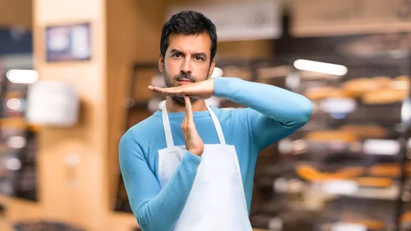 Man wearing an apron making stop gesture with her hand to stop an act in a bakery