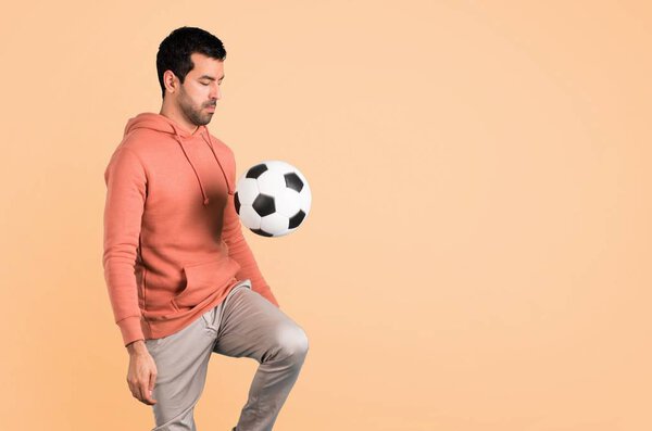 Man in a pink sweatshirt with soccer ball on ocher background