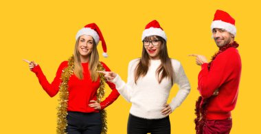 Parmak tarafına işaret ve sarı zemin üzerine gülümseyen bir ürün sunma Noel tatili için bir grup insanlar sarışın kadın giyinmiş