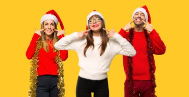 Üzerinde sarı arka plan ağız parmaklarıyla işaret ederken hoş bir ifade ile gülümseyen Noel tatili için bir grup insanlar sarışın kadın giyinmiş